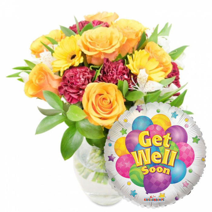 A comforting, cheerful gift set composed of a full floral bouquet in a clear glass vase and a glossy round Mylar balloon that proclaims Get Well Soon. The bouquet is placed slightly left of center and built around several generous, soft orange and deep yellow roses whose petals spiral outward, giving a classic, reassuring presence. Scattered among and around the roses are sunny yellow gerbera daisies whose broad faces add immediate brightness, while deep burgundy carnations introduce rich, shadowed texture that anchors the colour story. Slender sprays of white alstroemeria are woven through the mass of blooms, their tiny, freckled centers creating delicate punctuation and a sense of lightness. Abundant greenery-smooth, reflective leaves and finer filler foliage-cradles each bloom and imparts a freshly-cut garden aroma, visible through the clear vase that exposes neat stems and clear water. To the lower right, a shiny silver foil balloon partially overlaps the bouquet; printed at its heart is a lively cluster of cartoon balloons in bright purple, sky blue, lime green, hot pink and sunny yellow, some carrying stripes, polka dots or check patterns. The central wording Get Well Soon is rendered in cheerful yellow and blue with a soft shadow for depth, and small starburst graphics ring the white border; a tiny KALEIDOSCOPE mark appears at the very bottom edge. This arrangement radiates hope and warmth-ideal for sending to a friend or neighbour recovering at home in Stanmore, near Canons Park or the tube station, to brighten a hospital bedside or front-room table.