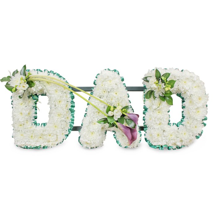 This photograph shows an elegant DAD funeral flower tribute created with the kind of meticulous care you might expect from experienced florists serving Stanmore and the nearby residential streets off Marsh Lane and Uxbridge Road. The three letters, D, A, and D, stand upright in a neat row against a pure white background, making every detail of the design easy to see. Each letter is crafted as a three-dimensional block and entirely covered with masses of pristine white chrysanthemums or similar small, rounded blooms. The petals overlap to form a dense, cushion-like surface, giving a sense of softness and serenity that suits a final farewell to a father. A rich emerald green satin ribbon runs around the entire perimeter of every letter, ruffled into gentle waves. This ribbon adds definition and frames the white flowers, its fresh green tone evoking the parkland around Bentley Priory and the tree-lined streets of Stanmore. Behind the blooms, slender dark bars hint at the supporting frame that keeps the tribute standing during the service.   

Extra floral details lend character and emotional nuance. On the top left curve of the first D, a delicate spray of white freesia and lush green foliage is nestled into the chrysanthemum base, the freesias rising above with their elegant buds and open flowers. From this point, two long, graceful green stems arch diagonally across toward the central A, creating a gentle line of movement across the tribute. At the meeting point on the A, an eye-catching spray features two deep purple calla lilies, their velvety trumpet shapes curling inward, surrounded by more white freesia blossoms and glossy leaves. This deeper shade of purple adds depth and solemn beauty to the composition. The final D is decorated at its upper right side with a smaller matching cluster of white flowers and greenery, tying the design together. The overall effect is one of calm dignity and heartfelt remembrance, a traditional yet deeply personal DAD tribute that families in Stanmore might choose to express love, gratitude, and lasting memories.