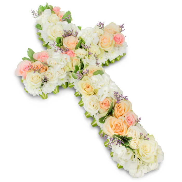 A reverent floral cross dominates the frame, its delicate pastel blooms standing out vividly against a pristine white background. The overall shape of the Christian cross is strong yet softened by the abundant flowers that conceal the underlying structure entirely. The base is densely packed with white and ivory blooms-roses, spray roses, hydrangea, and perhaps small chrysanthemums-arranged so closely that no gaps or stems are visible, lending the impression of a single, continuous layer of petals. Resting above this base, like gentle highlights, are clusters of roses in subtle shades of peach, apricot, and blush pink, their larger heads opening gracefully and providing focal points across the arms and centre of the cross. Interspersed among these roses, tiny accents of lavender-hued filler flowers add delicate points of cool colour, enhancing the design's depth and visual rhythm. Along portions of the cross's edges, slivers of fresh green foliage emerge, giving a natural border that gently defines the silhouette without disrupting the gentle harmony of the palette. The photograph's lighting is bright and even, capturing the creamy texture of the petals and the interplay of shadow where blooms overlap. It is easy to imagine this arrangement being carried into a church or chapel in Stanmore, perhaps for a service close to Bentley Priory or within a nearby parish, where families gather to say their final goodbyes. The floral cross conveys a sense of quiet devotion and respect, offering a tangible expression of faith, comfort, and enduring remembrance during times of mourning and reflection.