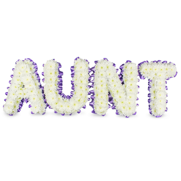 A meticulously constructed memorial piece spells 'AUNT' in large, elegant capitals, each letter densely composed of pristine white spray chrysanthemums whose tiny petals create a velvety, tactile surface. Here and there the chrysanthemums reveal pale yellow centers that lend a subtle sun-warm halo to the otherwise pure white heads, introducing a note of natural softness. Encircling each letter is a band of deep purple satin ribbon, deliberately pleated and slightly ruffled to form a decorative scalloped edge that contrasts with the smooth bloom faces and emphasizes the architecture of the letters. Under soft studio lighting, delicate grey shadows fall beneath the letters, revealing their three-dimensional frames and the careful build-up of flowers that lifts them from the white backdrop. The scent is understated-clean, green and faintly floral-evoking the calm presence that thoughtful sympathy flowers aim to offer. This arrangement balances precision and tenderness, designed for formal commemorations or private remembrances where an aunt's warmth and steady presence are being honoured. I picture it placed in a chapel on Stanmore Broadway or at a family service after a walk through Stanmore Common, offering both clarity of message and a quiet, supportive aesthetic. The colour pairing of immaculate white and dignified purple reads as both respectful and hopeful, an eloquent floral letter that communicates love, remembrance and the skilled hand of a local florist who understands the rituals of farewell.