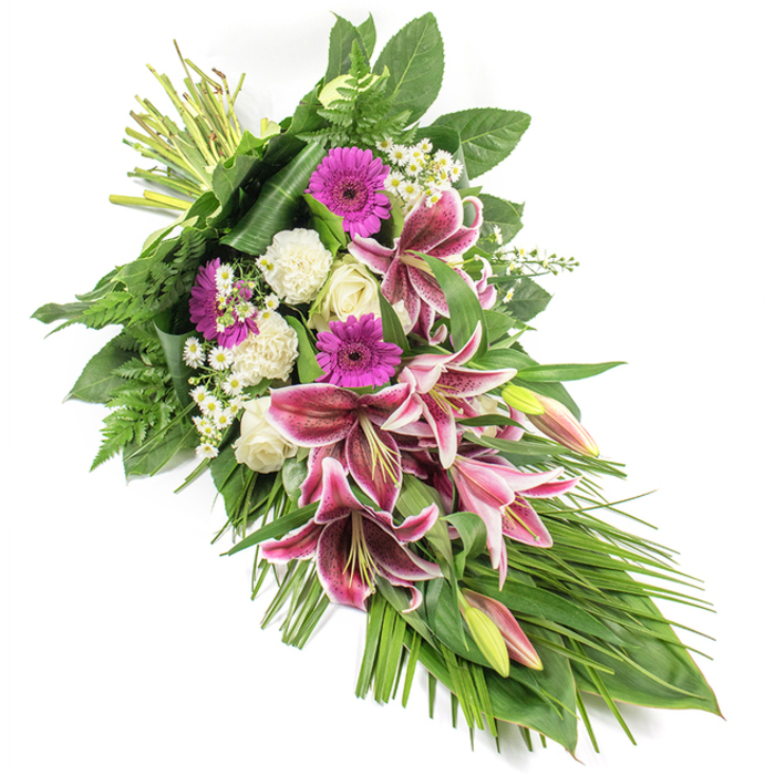 This detailed image shows a beautifully composed funeral sheaf laid out on a stark white background, allowing every blossom and leaf to be clearly seen. The arrangement stretches from the top left corner down to the bottom right in a graceful, elongated diagonal, giving it an elegant, teardrop-inspired silhouette. Dominating the centre are several dramatic Stargazer lilies, their star-shaped petals glowing with rich magenta and fuchsia tones, softened by pure white edges and fine burgundy speckles that mark the interior. Some lilies are fully opened, others remain as long buds tinged with pink and green, suggesting a gentle unfolding over time. Around them, vivid magenta gerbera daisies provide a contemporary pop of colour and warmth, while clusters of creamy white roses in bud and semi-open stages bring a traditional sense of purity and reverence. Ruffled white carnations flow throughout the spray, adding both volume and a soft, comforting texture. Tiny white daisy-like filler flowers, scattered lightly through the arrangement, add delicate accents and a feeling of lightness. The entire composition is surrounded by a lush framework of foliage: broad, dark green leaves form a strong foundation, feathery fern fronds contribute airy movement, and long, blade-like leaves extend outward and downward, emphasizing the shape and giving the spray a natural, cascading appearance. The stems are clearly visible and neatly tied at the top left, indicating a fresh, hand-crafted tribute, as though it has just been prepared at Flower Delivery Stanmore for a service near Belmont Circle or a memorial gathering close to Bentley Priory. The overall effect is serene and dignified, a heartfelt expression of sympathy and remembrance suitable for funerals and memorial services across Stanmore.