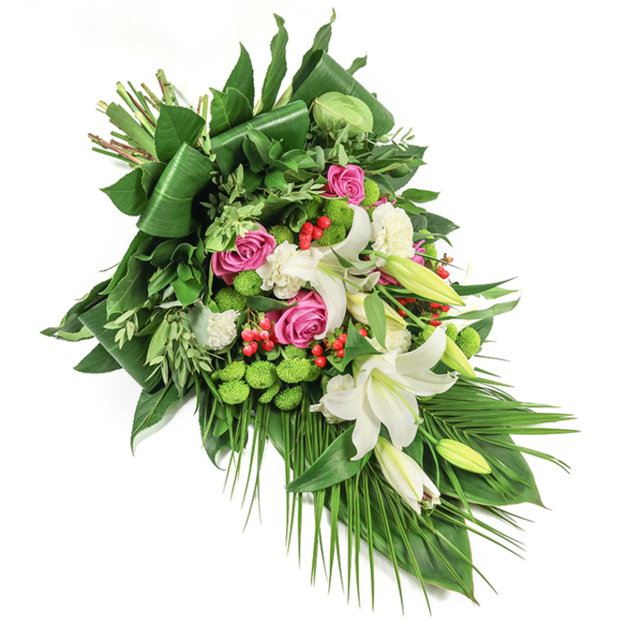 This thoughtfully designed sympathy spray, created by Flower Delivery Stanmore, stretches gracefully in a diagonal arc across a pure white background, displaying a careful blend of classic blooms and modern greenery. Dominant within the arrangement are voluptuous white lilies, their satiny petals either wide open with golden stamens visible or elegantly poised as unopened buds-each signifying peace and the ongoing nature of love and remembrance. Weaving through the lilies are clusters of deep pink and fuchsia roses, each at various stages of bloom, providing depth, vibrancy, and heartfelt sentiment akin to moments spent amid the floral displays at Stanmore Country Park. Accents of ruffled white spray carnations and distinctive, rounded lime-green santini chrysanthemums contribute layers of texture and visual delight, while scarlet red hypericum berries provide striking contrast and points of interest. The spray is anchored by broad, glossy greens folded for structure, with softer, feathered leaves and palm fronds cascading elegantly down, echoing the natural topography of Stanmore's open spaces. Soft, ambient light enhances the purity of the white blooms and the lively interplay of rose and green, forming an atmosphere of comfort and respect. Ideal for funeral and memorial services in Stanmore, this lush tribute embodies both serenity and the skilled craftsmanship of local florists honouring loved ones' lives.
