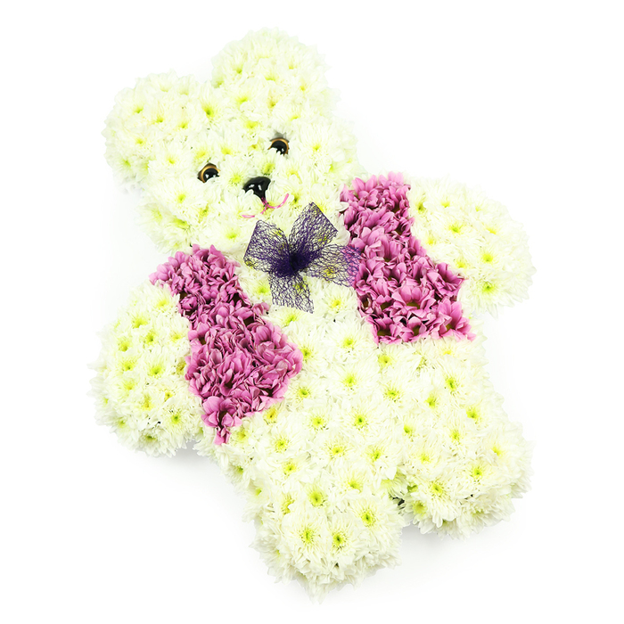 The photograph presents a meticulously designed teddy bear floral tribute, captured against a plain white backdrop that lets the gentle colours and textures speak for themselves. The bear's body is fully cloaked in layers of creamy white chrysanthemums, each flower head nestled tightly against the next to create the illusion of soft, fluffy fur. The rounded head, clearly defined ears, and slight curve of the belly give a sense of three-dimensionality, as though the bear is sitting upright on an invisible base. At the centre of the face, two small dark blooms represent the eyes, placed carefully so they convey a kind, almost watchful expression. A diminutive dark nose sits just below, while the subtlest curve suggests a quiet, reassuring smile. Across the chest, a decorative waistcoat effect is achieved using rich pink, mauve, and lilac blooms-likely hydrangeas and co-ordinating chrysanthemums-arranged in two symmetrical blocks. These coloured flowers add character and contrast, creating a playful yet dignified accent. Finishing the design, a small bow made from sheer violet netting rests neatly at the neckline, its transparent loops and tails introducing a light, graceful movement. The absence of greenery keeps the composition clean and focused, with the soft, even lighting emphasising the freshness of the petals and the skillful workmanship. In Stanmore, this style of teddy bear tribute is often chosen by families saying farewell to a child, grandchild, or someone closely associated with childhood memories, whether the service takes place near Stanmore Hill, in a local church, or at Breakspear Crematorium. It captures the innocence and tenderness of a beloved toy, translated into flowers that offer comfort and quiet remembrance.