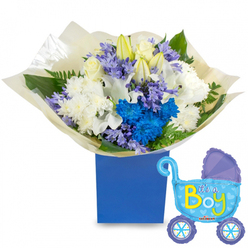 This celebratory bouquet reads like a gentle announcement: a lush, rounded arrangement presented in a sturdy royal blue rectangular gift box, its palette built around crisp whites, soft lavenders and a striking electric blue that unmistakably signals a joyful welcome for a baby boy. White roses nestle into the centre, accompanied by elegant white lilies-some still in bud-whose long, satiny petals promise unfolding days ahead. Surrounding them, full white chrysanthemums add volume and a cloud-like softness, while clusters of electric blue chrysanthemums and smaller cornflower-to-periwinkle blossoms weave through the composition, creating dynamic contrast and a subtle textural chorus. Greenery-broad dark leaves and delicate fern fronds-splays outward, adding a fresh, garden-picked frame and catching the light on each glossy surface. The bouquet is wrapped in crinkled cream tissue that gathers at the base, lending a handcrafted, tactile quality as the paper rustles softly when handled. To the right, a cheerful, light blue baby-carriage foil balloon bobs slightly, its canopy and wheels trimmed in darker blue and punctuated with polka dots and hearts; across its side, bright yellow and green lettering spells out "It's a Boy." The image conveys quiet joy and thoughtfulness-a perfect hospital visit or homecoming gift for new parents in Stanmore, Pinner or nearby Harrow, carrying the kind of tender craftsmanship you'd expect from a neighbourhood florist handling a newborn celebration.