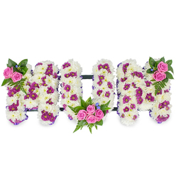 A lovingly crafted floral tribute spelling out MUM in bold three-dimensional letters, set on a clean white backdrop so every petal and colour speaks clearly. Each letter is constructed from a thick, velvety carpet of white chrysanthemums, their small, curled petals forming a plush, tactile surface that reads as softness and reverence. Throughout the white base, isolated pockets of deep purple or magenta spray chrysanthemums add a quiet rhythm and depth, while clusters of bright pink spray roses act as warm, heartfelt focal points. The left M bears a modest cluster of two or three pink roses at its top left, framed by rich green foliage and delicate fern fronds with a few tiny blue accents nesting amongst the leaves. The central U hosts a larger, more composed bouquet - roughly four to five pink roses arranged within its lower curve, surrounded by lush greenery that suggests shelter and embrace. The right M responds with a mirrored rose cluster at its upper right, giving the whole arrangement a balanced, symmetrical sentiment. Thin, dark bars run subtly between the letters to keep the piece unified and stable without detracting from the floral surface. In gentle, cool light the white mums read as almost luminous, their texture contrasting with the glossy rose petals; the ensemble exudes quiet affection and remembrance. This bespoke design is suitable for a funeral service or memorial in Stanmore, whether delivered to a chapel near Canons Park or to a family home on Stanmore Broadway, and is the sort of careful, considered tribute we create at Flower Delivery Stanmore for those seeking dignity and tenderness in bereavement.