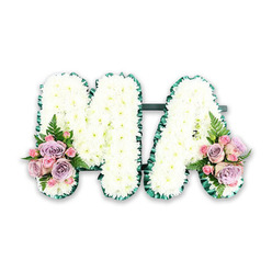 This elegant funeral floral tribute spells out the letters M and A in large capitals, combining traditional white sympathy blooms with soft pastel accents for a gentle, comforting effect. Each letter is fully covered in small white chrysanthemums, placed so closely that they form an unbroken blanket of petals, with each flower head facing outward to catch the light. The chrysanthemums create a soft yet structured surface, giving the impression of something both tender and steadfast-much like the memory of a cherished mum. Around the edges of the letters, a rich green satin ribbon is carefully ruffled, producing a delicate pleated trim that outlines the M and A with clarity. The green edging not only frames the flowers but also symbolises life and renewal, subtly balancing the purity of the white blooms. A slim connecting bar, also in green, holds the letters together as a single tribute. At the base of the left leg of the M and the right leg of the A, two matching flower sprays add colour and emotional warmth: lilac roses, pale pink roses, and smaller pink spray roses gathered in tight clusters, with a feathery fern frond lifting the design and adding depth. The tribute is photographed on a plain white backdrop, similar to how it might appear in a Stanmore florist's studio before being delivered to a local crematorium or placed gently at a graveside in the surrounding area. Soft, dignified, and unmistakably personal, this MA arrangement offers families a simple yet deeply meaningful way to honour the life and love of a special mother figure.