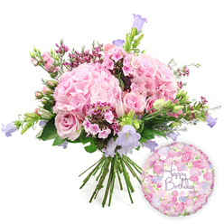 Set against a pure white studio backdrop, this image shows a generous birthday bouquet and coordinating foil balloon, arranged as if ready to be carried out of a Stanmore flower shop for delivery. At the centre, several large, rounded heads of pale blush hydrangea form a soft, voluminous base. Their many delicate petals overlap so densely that the flowers resemble fluffy clouds of pink, inviting the eye and suggesting a plush texture. Nestled within these hydrangea mounds are soft pink roses, some in full, layered bloom revealing their spiralling hearts, while others remain in firm, elegant buds, waiting to open on a windowsill overlooking Stanmore Hill. Sprinkled throughout the arrangement, small clusters of vivid fuchsia-pink filler flowers, similar to waxflower, provide tiny bursts of deeper colour and fine, intricate detail. Slender stems of campanula emerge gracefully from the main dome, each bearing bell-shaped blooms in gentle lavender and periwinkle hues that arc delicately upward, bringing cool, airy tones into the predominantly pink palette. A frame of lush greenery surrounds the flowers-slender pointed leaves, broader foliage, and fresh, upright stems-adding structure and echoing the leafy streets around Stanmore Park. The bouquet's stems are clearly visible at the base, neatly gathered and slightly splayed, emphasising the hand-tied, freshly cut nature of the design. To the lower right, a round foil balloon with a subtle metallic sheen catches the light. Its surface is patterned with tiny roses and buds in soft pink, cream, and lilac, arranged around the words "Happy Birthday" written in an elegant purple script. Together, the abundant flowers and balloon evoke warmth, joy, and thoughtful celebration, ideal for a birthday breakfast at home, a party hall near Stanmore station, or a surprise doorstep delivery anywhere in the local area.