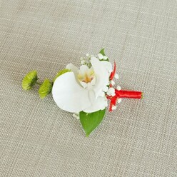 A refined wedding boutonniere lies carefully placed on a pale beige linen-like cloth, its slightly coarse weave providing a calm, natural backdrop that recalls relaxed gatherings in Stanmore's leafy residential streets. The focal point is a flawless white phalaenopsis orchid, its large, smooth petals spreading in soft arcs, catching the light with a gentle satin sheen. At the centre, the orchid's throat reveals a nuanced blend of buttery yellow and subtle reddish-brown markings, drawing the eye inward with painterly detail. Surrounding this central bloom, clusters of tiny, cloud-like white baby's breath add an ethereal softness, like a light mist over the playing fields near Canons Park. To the left, two compact lime-green chrysanthemum pom-pom buds bring a contemporary edge, their tight, spiky texture offering a vivid contrast to the orchid's calm elegance and providing a fresh shot of colour. A broad, rich green leaf curves beneath the blooms, with a smaller, darker leaf tucked near the stem, giving the design depth and a sense of natural balance. The stems are tightly wrapped in a striking crimson red ribbon, the satin fabric glinting gently under soft, diffused light and tied into a precise bow or firm knot that speaks of practiced hands and attention to detail. Every element of the arrangement-colour, form, and texture-feels intentional, evoking a sense of poised celebration suitable for a groom, groomsman, or formal guest arriving at a wedding in Stanmore. The overall mood is quietly luxurious and deeply personal, like a final, heartfelt flourish added just before stepping into the aisle.