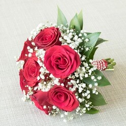 Brimming with elegance reminiscent of gatherings at Bentley Priory or bridal moments at Stanmore Country Park, this luxurious bouquet is anchored by a collection of velvety red roses at their most striking bloom. Each petal is carefully curved and layered, spiraling outward in dramatic crimson waves that speak of enduring love and sophistication. Interspersed with liberal clouds of delicate, snowy white baby's breath, the arrangement is both passionate and ethereal, each Gypsophila flower lending a dreamlike, celebratory texture. Fresh green leaves with a glossy finish-possibly ruscus or salal-emerge here and there, framing the roses and offering a sense of organic abundance. The bouquet's stems are gathered and wrapped in a festive red-and-white striped ribbon, further adorned with a winding thread of lustrous pearls, a signature flourish from a skilled Stanmore florist's hands. Resting softly on a light, textured fabric background, the composition is bathed in even, natural light to accentuate the vibrant red, white, and green hues. Whether meant for a wedding party, a special anniversary, or a gesture of deep affection, this bouquet reflects the heartfelt emotions and time-honoured floral artistry cherished within Stanmore's elegant community.