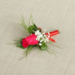 A delicately crafted boutonnière featuring a single deep fuchsia rosebud rests on a neutral, light beige fabric background that resembles finely woven linen, its texture gently visible beneath the flowers. The rosebud is tightly closed yet full-bodied, with layers of smooth, velvety petals spiralling inward, the outer edges a vivid pink that deepens to a more intense magenta at the centre. Encircling the rose are fluffy clusters of baby's breath, each tiny white flower like a soft pearl, creating a misty, romantic frame that contrasts beautifully with the richness of the rose. Slender, bright green foliage radiates from behind the blooms, some strands thin and feathery like ornamental grass, others slightly broader, adding both structure and an airy, natural movement, as though freshly snipped from a Stanmore garden near Canons Park or along The Broadway. The stems are neatly aligned and tightly wrapped in a lustrous red satin ribbon, the wrapping perfectly smooth, ending in a subtle loop that provides a refined finishing touch. Gentle, even lighting falls across the scene, illuminating every petal vein, the matte softness of the baby's breath, and the satin sheen of the ribbon, giving the impression of a freshly made piece ready for same-day collection or delivery around Stanmore. The overall mood is quietly joyful and romantic, ideal for a groom standing outside a local Stanmore church, a prom date waiting by the station, or anyone wanting a traditional, handcrafted lapel flower with a modern pop of colour. The image captures the intimate artistry of boutonnière design, where each detail is chosen to enhance a single, perfect rose.