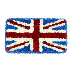 A rectangular floral panel depicts the Union Jack in exquisite detail, crafted as a funeral or memorial tribute and photographed against a bright white background that heightens the impact of the colours. The flag is built entirely from small, tightly packed flower heads, creating a dense, cushion-like surface that appears soft to the touch. Deep, velvety blue blooms form the base of the design, filling the outer sections and corners so the central crosses seem to sit proudly on top. Across this blue field, the broad red bars of St George's Cross cut a confident path vertically and horizontally, their rich crimson petals packed closely together so the lines remain strong and unbroken. Diagonal red bands, forming St Patrick's Cross, span from corner to corner, each one bordered neatly by slender white lines made from petite, pure-white flowers. These white flowers also create the wider diagonals of St Andrew's Cross, giving a cool, luminous contrast to the surrounding reds and blues. The floral texture creates subtle shadows and highlights, adding depth and movement to what is essentially a flat tribute, as if the flag has been gently smoothed out for a final moment of respect. This design feels perfectly suited to a British remembrance service, perhaps in Stanmore after a ceremony at a local church or synagogue, where families gather to honour a life of service or deep national pride. The arrangement's balance of precision and softness speaks to the kind of thoughtful, careful work local florists bring to important farewells.