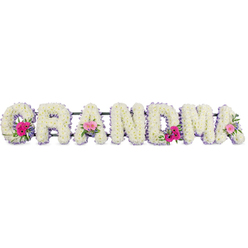 This funeral flower display shows the word "GRANDMA" arranged in large, reassuring letters, each one completely enrobed in crisp white chrysanthemums. The chrysanthemums are placed so closely together that they form a smooth, plush surface, their rounded petals giving a sense of softness and purity. A neat trimming of pale lilac ribbon outlines each letter, following every curve with a gentle, satin glow that adds refinement and a hint of delicate colour. Interspersed along the tribute are small floral posies, featuring bright pink gerberas and soft pink roses, supported by sprigs of natural green foliage. These miniature bouquets bring life, contrast, and a feeling of affectionate celebration, like cherished stories picked out in brighter tones. The light in the image is calm and flattering, illuminating the flowers without glare and allowing the whites, pinks, and greens to blend harmoniously. It is easy to imagine this tribute resting at a service in Stanmore, perhaps on a stand near the altar or by the catafalque at a local crematorium, where family members might pause and reflect. For a florist serving the Stanmore community, such a piece speaks to careful craftsmanship: the letters are well-defined, evenly filled, and beautifully balanced. The floral lettering does more than name a relationship; it becomes a heartfelt symbol of love, remembrance, and the enduring bond between a grandmother and her family.