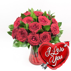 A romantic still life unfolds against a crisp white background: a lush bouquet of red roses gathered in a ruby-red glass vase, accompanied by a gleaming heart-shaped balloon that proudly declares "I Love You." The roses, numbering around a dozen or a little more, are arranged closely together so that their heads touch and overlap, forming a domed canopy of velvety petals. The blooms show subtle variation in size and openness, some tightly coiled at the centre, others generously unfurled to reveal intricate swirls of rich crimson. Interspersed among the flowers are deep green leaves, their smooth, slightly waxy surfaces catching hints of light, adding texture and volume to the bouquet in the same way the mature foliage frames the quiet residential roads of Stanmore. The flowers sit in a clear, fluted vase made from ruby-tinted glass. Its vertical ridges run from base to rim, creating narrow channels of brightness where the light strikes. The stems inside crisscross in the softly coloured water, giving a sense of natural, hand-crafted arrangement. To the lower right of the vase, overlapping its base, a metallic red heart-shaped foil balloon adds a jubilant, modern touch. Its shiny surface reflects the surroundings in soft distortions, and across the centre of the heart the phrase "I Love You" appears in elegant white cursive, easy to read and emotionally direct. A stylised silver arrow slices diagonally through the heart, echoing traditional Cupid imagery. With no additional props or background elements to compete for attention, the composition feels focused and intentional, a perfect visual for a Stanmore couple celebrating Valentine's Day, a milestone anniversary, or a meaningful date night.