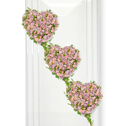 In this image, three heart-shaped clusters of roses descend gently across a bright, white backdrop, forming an elegant cascading funeral tribute. The hearts are filled edge to edge with small roses in hushed, romantic tones of dusty lavender, soft mauve, and pale pink. Each rose is placed precisely, their layered petals overlapping to create a sumptuous, velvety surface, with buds in different stages of opening that bring depth and natural rhythm to the design. The hearts follow a diagonal path from upper left to lower right, each one slightly overlapping the next, so the eye travels along them as if tracing a quiet journey of love and remembrance. Intertwining around the outer curves of the hearts and flowing between them are delicate strands of ivy, the leaves a rich, glossy green that gently outlines the shapes and links them together. This foliage adds structure and a sense of connection, suggesting family, friendship, and bonds that cannot be broken by distance or loss. The clean white background features faint, vertical reflections reminiscent of a window, a polished wall, or a serene chapel near Stanmore's leafy streets and open spaces. This neutral setting allows the soft rose colours to glow, creating a calm, contemplative mood. It is the sort of considered, symbolic tribute a local Stanmore florist might design for a funeral or celebration of life, a piece that quietly communicates devotion, unity, and cherished memories shared over the years.