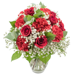 A richly coloured bouquet of red and white flowers is displayed in a clear glass vase, set against a crisp white background that makes the colours almost glow, evoking the calm elegance of a Stanmore home ready for a special celebration. The dominant blooms are velvety deep red roses, their tightly layered petals curling inward in smooth spirals, some just beginning to open as if caught in a moment of quiet anticipation. Interspersed with them are full, ruffled red carnations, their abundant layers of petals forming plush, rounded shapes that lend the arrangement a generous and comforting fullness. Threaded throughout the composition is an airy haze of white baby's breath, the countless tiny blossoms forming a delicate veil that softens and brightens the bold reds, much like sunlight filtering across the open spaces of Bentley Priory Nature Reserve. Rich green foliage weaves in and out between the blooms, with glossy dark leaves and softer, rounded eucalyptus in a muted silvery green adding depth, movement, and a touch of natural calm. The stems are gathered neatly within a simple clear vase, its gently flared rim and sturdy base allowing the viewer to see the straight green stems and clear water inside, suggesting freshness and expert florist craftsmanship from the local Stanmore specialists. The bouquet is arranged into a rounded dome, balanced and full without feeling heavy, exuding a timeless romantic charm. It feels perfect for an anniversary dinner at home near Stanmore Broadway, a Valentine's surprise delivered across HA7, or a heartfelt gesture of appreciation, where classic red and white flowers quietly express love, admiration, and sincere emotion.
