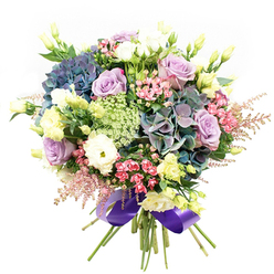 A beautifully orchestrated tableau of blooms, this Stanmore bouquet shimmers with detail and thoughtful artistry, its palette of blues, violets, and creamy whites forming a serene tribute to the area's timeless elegance. At its foundation, generous balls of hydrangea radiate regal indigo and gentle teal, echoing the tranquil tones of Stanmore's tranquil parks after a spring rain. Interlaced are soft lavender roses and classic white ranunculus, their spiraling petals giving the bouquet an unmistakable air of romance and refinement. Interspersed throughout, slender eustoma buds add lightness and a slight blush of sunshine, offset by flourishes of vivid fuchsia-pink and feathery astilbe that ripple through the design with playful movement. Delicate lace-like filler flowers bring a subtle wildflower charm reminiscent of walks along the Stanmore trails. Enveloping all, broad dark green leaves provide a sturdy yet vibrant backdrop. The arrangement is artfully hand-tied and finished with a sumptuous royal purple satin ribbon-its sheen mirroring the understated luxury of Stanmore's grand homes. Designed for celebrations, anniversaries, or any moment deserving a lavish flourish, this bouquet captures the warmth, skill, and creative flair of local Stanmore florists, fresh and ready for delivery throughout the area.