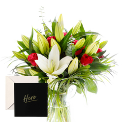 This bouquet embodies refined elegance and emotion, composed to evoke admiration and comfort in equal measure. The white lilies sit central, their trumpet shapes and creamy petals glowing as they rise above abundant green spears and curling foliage. Red roses weave through the arrangement, their velvety blooms perfuming the air with a classic, intimate sweetness. The many unopened buds promise future beauty, hinting at ongoing celebration and hope. Bathed in bright, natural light, the bouquet feels fresh and lucid, each leaf and petal outlined with crisp, honest detail. An elegant card marked Hero accompanies the flowers, making this gesture well suited for expressions of thanks, remembrance, or encouragement for someone who has inspired others. In Stanmore, this arrangement would grace a quiet home near the High Street or beside a warmly lit hallway, offering both solace and celebration. It's a reliable choice for birthdays, milestones, or simply to show someone they are valued. The delivery service across Stanmore ensures fresh, punctual arrival, keeping stems cool on the journey and preserving fragrance as they travel from studio to doorstep. On a weekend stroll along Canons Park or Stanmore Hill, this bouquet would lift the mood of any entry and reflect the care of a local florist.