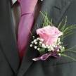 There's a gentle lyricism in this Stanmore boutonniere-a pink rose blooming fresh at its centre, its satiny petals alive with blush and possibility. Encircling it, feather-light sprays of baby's breath impart a sense of serenity and hope, their white blossoms floating above the rose like morning mist on Stanmore Recreation Ground. Drawing the ensemble together are wispy, vibrant greens and a deep lavender satin ribbon that glistens in the light. Resting on the lapel of a charcoal suit, with a fuchsia tie and patterned pale grey shirt completing the look, the arrangement feels both classic and utterly suited to contemporary celebrations in Stanmore. Crafted by skilled hands, this floral accent weaves together colour, tradition, and the spirit of community-making it an ideal choice for those marking cherished milestones, and a reminder that every detail, no matter how small, can hold the joy and promise of a new beginning.