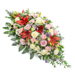 A long, double-ended coffin spray rests against a bright white background, its generous length and symmetry making it ideal for placement along the top of a casket during a Stanmore funeral or memorial service. The arrangement is lush and full, densely packed with a variety of flowers in tones of deep red, creamy white, and delicate pinks, softened with hints of lavender and purple. At its heart are vibrant red Oriental lilies, their large, star-like blooms spreading open with a sense of quiet drama, symbolising strength and heartfelt devotion. These are surrounded by clusters of pale cream and blush pink roses, some in tight buds that hint at newness, others fully opened in layered spirals, their velvety petals bringing tenderness and warmth. Light pink spray carnations are threaded throughout, their softly ruffled petals adding volume and a cloud-like softness. Between the larger blooms, subtle filler flowers in shades of lilac and light purple peek through, gently deepening the colour palette without overwhelming it. All of the flowers are cradled in a generous bed of dark green foliage, including broad, glossy leaves that give structure and finer, trailing greenery that softens the edges and enhances the elongated, double-ended shape. The spray feels balanced and considered, designed to be viewed from every angle and to sit comfortably in a chapel or crematorium setting around Stanmore and nearby Bushey. It conveys a message of profound sympathy and remembrance, the kind of floral tribute that quietly supports a family through their final farewell, embodying both respect and enduring love in its rich yet soothing composition.