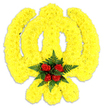 A meticulously sculpted floral tribute takes the unmistakable form of the Khanda, the Sikh emblem, crafted from a dense carpet of bright yellow chrysanthemums that follow the emblem's sweeping curves and bold lines. The circular chakkar, the central double-edged khanda and the two crossed kirpans are all rendered in tightly packed, sunlit yellow blooms whose layered petals create a soft, plush surface and a subtly three-dimensional silhouette. At the focal point where the circular element meets the blade, a compact cluster of five deep red roses is nestled, their velvety petals turned gently outward and cushioned by a rosette of dark green fern fronds that frame the crimson centre with cool, textured foliage. The composition sits against a clean white background; a soft grey shadow beneath it confirms this is a physical memorial piece-likely foam- or board-mounted-meant to stand alone as a wreath or table tribute for a funeral, memorial service, or religious celebration. Light plays across the chrysanthemums' ruffled surfaces, catching highlights on individual petals and deepening the contrast with the roses, while the scent, though faint in the photograph, can be imagined as a quiet mix of green fern and gentle floral sweetness. This arrangement reads as a careful expression of respect and cultural reverence, made with the kind of craftsmanship a local Stanmore florist would deploy for a service near Canons Park or along Stanmore Broadway, where community and tradition are held close and colour is used with clear intent to comfort and honour.