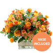 Set against a stark white background, this warm-toned floral arrangement shines like a small sunrise, its colours echoing the soft oranges and yellows you might see over Stanmore's rooftops on a clear morning. At the centre, open orange roses reveal layers of velvety petals that fade gently from vivid tangerine at the tips to a mellow, honeyed yellow near the core, giving the impression of light radiating outward. Interspersed among them are neatly rounded yellow garden roses, tightly furled and full of texture, their many petals creating tidy, symmetrical rosettes. Between the larger blooms, clusters of peach and light orange alstroemeria, or Peruvian lilies, stretch out on slender stems, each flower displaying delicate speckles and striping that add fine, decorative detail. Dotted throughout the bouquet are small, intensely spiky orange spheres, reminiscent of safflower or thistle flower heads, which lend energy and a slightly playful, textural twist. The arrangement is framed by a collar of foliage in varied greens, including silvery eucalyptus leaves and darker green fillers, adding depth, contrast, and a sense of natural abundance. All the stems are carefully placed into a clear, square glass vase, its simple geometric form highlighting the vertical lines of the stems and the clarity of the water inside, suggesting freshly prepared flowers, ready for delivery across Stanmore. Wrapped snugly around the vase's centre is a band of natural beige burlap or jute, its rustic texture softening the sleek glass and evoking a hand-tied, artisan feel that would look at home on a kitchen island off London Road or in a lounge near Stanmore Golf Course. In the bottom right corner of the image, a bright circular orange badge carries the message VASE INCLUDED in bold white capital letters, confirming that the display arrives as shown. The overall effect is one of cosy brightness and gentle celebration, perfect for marking milestones, offering thanks, or simply bringing a welcoming glow into a Stanmore home.