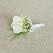 A single white orchid boutonniere is laid carefully on a softly textured, light beige fabric that looks like finely woven linen, its natural threads catching the gentle, even light. At the heart of the design sits a pristine Phalaenopsis orchid bloom, its broad, velvety petals a pure, creamy white that almost glows against the neutral backdrop. In the centre of the flower, the throat reveals a subtle wash of pale yellow, a quiet warmth that suggests freshness and delicate fragrance. Surrounding the orchid, clusters of tiny white baby's breath flowers create a cloud-like halo, each miniature bloom adding a sense of softness, romance, and airiness. Threaded between these dainty blossoms are slender strands of vibrant green foliage, possibly an airy fern or similar fine greenery, whose feathery tips bring a fresh, garden-picked feel to the otherwise polished piece. The stems are neatly gathered and wrapped in a smooth white satin ribbon, the fabric folded with care and finished in a small, understated bow that signals expert florist craftsmanship. The neutral oatmeal-toned background lets every white and green detail stand out without distraction, evoking the feeling of a calm bridal morning in Stanmore, perhaps moments before a ceremony at a local church or a reception near Stanmore Country Park. This elegant boutonniere, with its modern orchid and traditional baby's breath, is captured as if waiting to be pinned to a groom's or groomsman's lapel, radiating quiet sophistication, purity, and the promise of a joyful celebration shared with family and friends nearby.