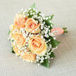 Imagine a bridal posy whose first impression is whisper-soft romance: peach roses clustered at the core, each petal edged with creamy luminosity and folding into a tender centre. Surrounding them, a froth of white gypsophila creates a delicate veil that softens edges and scatters the light, giving the bouquet a haloed quality. Sprigs of glossy green foliage anchor the design and add contrast, so the peach tones read warmer and more distinct. The stems are neatly wrapped in peach satin ribbon, the finish punctuated by a string of small pearls that catch the light like thoughtful mementos. You can almost sense the cool, velvety texture of the roses beneath your fingers and the faint, fresh scent that suggests a morning garden rather than heavy perfume. This bouquet was conceived with careful proportion and a gentle silhouette, intended to sit naturally in a bride's hands without overpowering her gown. It photographs warmly in soft daylight - the kind that filters through trees at Canons Park or across a churchyard near Marsh Lane - and feels equally at home on a registry table or as part of an understated reception décor. The arrangement speaks to beginnings and steady affection, combining classic materials and florist craftsmanship to create a piece that is both stylish and quietly sentimental.