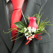 This intimate view of a handcrafted boutonnière reveals the quiet artistry behind many wedding mornings in Stanmore. The main attraction is a beautifully shaped hot pink rose, its petals unfolding in elegant, overlapping layers that cradle the centre like a gentle embrace. The colour is vivid yet sophisticated, carrying tones of fuchsia and rose that speak of affection and heartfelt celebration. Surrounding the central bloom is a fine ring of baby's breath-clusters of tiny, star-like white flowers that provide a soft counterpoint to the smooth, generous curves of the rose petals. Their airy presence feels like a whisper of cloud, light and almost weightless. Fine strands of ornamental grass arc around the rose, their slender form adding an understated sense of movement, as if they had caught a light breeze wafting across Stanmore's open spaces on a clear morning. A single, deep green leaf forms the backdrop, its smooth, waxy surface lending structure and allowing the pink and white elements to stand out in sharp relief. At the base, a neatly tied red ribbon holds everything together with quiet confidence, echoing the reds often seen in ties, sashes, or table arrangements at receptions near Stanmore Golf Club or local venues along the High Street. Resting against a dark suit, the boutonnière feels fresh and intentional, a refined finishing touch rather than an afterthought. One can almost sense the coolness of the rose against the fingertips and the soft, clean fragrance that rises when the bloom is pinned on, ready to accompany the wearer through each important moment of the day.