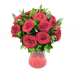 A generous bouquet of roughly a dozen to fifteen deep red roses is gathered in a rounded, almost domed shape, displayed in a translucent ruby glass vase set against a pure white studio background. Each rose is fully open yet still structured, with velvety petals spiralling out from the centre in classic, layered whorls that give the blooms a plush, luxurious texture. The red is intense and saturated, leaning towards rich crimson, and it catches the light so that the outer petals appear slightly darker while the inner curls glow with a softer, almost ember-like warmth. Between the roses, clusters of dark, glossy green foliage-likely ruscus-emerge, the pointed leaves adding contrast, depth, and a slightly wilder, garden-fresh edge to the otherwise polished design. The vase itself is a key part of the composition: its glass is tinted in the same red family as the flowers, with a gently flared neck and a curving body that narrows towards the base, subtly ribbed or waved so it reflects highlights and shadows like ripples on water. Because the glass is semi-transparent, hints of stems and deeper tones can be seen within, tying the whole arrangement together tonally. The white background removes any distraction, making this bouquet the single, powerful focal point-an image that feels intensely romantic and intentional. It calls to mind a heartfelt delivery arriving at a home near Stanmore Hill or a quiet side street off The Broadway, perfect for anniversary surprises, Valentine's Day declarations, or any moment when someone in Stanmore wants to send love in its most traditional, unmistakable form: a dozen red roses displayed with elegant simplicity and emotional clarity.