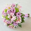Designed in Stanmore for moments that matter, this lush, hand-tied bouquet brings together romance, freshness, and expert artistry. At the heart are voluptuous lavender roses, their spiraled petals embodying tenderness and refined style-perfect for bridal celebrations at Stanmore's elegant venues. Bright lime green Santini mums gather in lively pockets around the arrangement, their round, compact blooms contrasting beautifully against the gentle pastels. Pink Alstroemeria lilies introduce an airy, whimsical note, their petals arched gracefully, tinged with soft gold and streaked with passionate pink, reminiscent of springtime in local parks or a stroll past bustling Stanmore shops. Sprigs of baby's breath thread throughout, forming a delicate, cloud-like veil, while glossy green leaves edge the bouquet with richness. The stems are encased in lustrous fuchsia satin ribbon, finished with a slender, shimmering string of pearl beads-a detail beloved by many Stanmore couples. Framed against a subtly textured, ivory surface, the bouquet's joyful palette and plush textures evoke the artistry and warmth of a Stanmore florist, ready to bring beauty to any celebration or heartfelt moment.