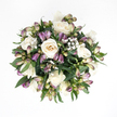 From a bird's-eye view, this sympathy bouquet rests on a bright white background, its rounded form and gentle colours creating an impression of calm and composure. At its core, several creamy white roses bloom in full, their petals soft and velvety, unfolding in elegant spirals that reveal a delicate ivory and slightly peach-tinted centre. A few roses remain more tightly formed, their petals hugging close, lending a feeling of quiet introspection. Threaded among them are purple alstroemeria buds, slender and slightly arching, their pointed tips shaded in tones of lavender and subtle plum, merging into pale green and faint pinkish hues near the base of each bud. Some are just beginning to show a sliver of inner petal and the first hint of fine striping, suggesting beauty that continues to unfurl over time. Delicate sprigs of baby's breath are woven throughout, each branching stem sprinkled with many tiny white flowers that create a soft, mist-like effect, gently linking each larger bloom. Surrounding this mix is a band of deep green foliage, the leaves broad, smooth, and lightly glossy, curving around the flowers to shape a neat, spherical outline. The soft, even lighting enhances the bouquet's tranquil character, reminiscent of the natural daylight in a Stanmore home near Canons Drive on a quiet afternoon. It feels like an arrangement chosen to offer comfort and sympathy within the Stanmore community, suitable for a condolence visit on a residential street off Uxbridge Road or as a thoughtful tribute at a modest memorial gathering, sharing a message of peace, purity, and gentle remembrance.