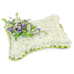 A comforting sympathy pillow composed almost entirely of hundreds of small, pristine white chrysanthemum heads, arranged so densely they read as a single, soft, cloudlike surface. The shape is a gentle rectangular cushion with rounded corners and a slightly raised, puffy profile, crafted to suggest rest and peacefulness. Around the entire edge a delicate light-green ribbon trim has been pleated into neat, overlapping scallops, producing a fresh, tender frame that lifts the white mass and gives the piece a subtle definition. Anchoring the design in the upper-left corner is a small spray of accent blooms: soft white lisianthus petals sit beside deep purple lisianthus - some open, some still in tight buds - their cool violet tones offering a respectful, consoling contrast. Fine fern fronds and slender green foliage weave through the cluster, adding air and texture while a broad dark-green leaf wrap secures the stems beneath, keeping the composition tidy and refined. The scent is quietly floral and green-lifted notes of chrysanthemum with the ephemeral sweetness of lisianthus-evoking calm rather than show. The arrangement is photographed against a clean white background with a faint drop shadow that emphasizes its three-dimensional form, much like a tribute set gently on a chapel table or graveside mound. As a local Stanmore-style memorial piece, it reads as both classic and personal: pure whites for peace, purple for dignity, and the lime-green trim suggesting renewal. An experienced florist's hand is evident in the symmetry, the tight packing of blooms, and the restrained use of colour to convey consolation and lasting care.