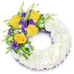 A respectfully crafted sympathy wreath formed as a perfect circular 'O', photographed against a clean white backdrop so every detail reads clearly. The body of the wreath is built from hundreds of small, pristine white spray chrysanthemums tightly packed to form a soft, cloud-like ring; their layered, feathery petals overlap to create a smooth, pillowed texture that reads of calm and purity. Nestled on the upper left curve is a concentrated spray of colour: several fully opened yellow roses with buttery, unfurling petals that catch the light, paired with deep, velvety purple lisianthus whose ruffled, cup-shaped blooms add a cool, dignified contrast. A scattering of smaller lisianthus buds in pale lavender and green gives the cluster natural depth, while glossy green foliage - rounded salal-like leaves, delicate fern fronds and mixed variegated greens - frames the blooms and lifts them slightly away from the white base. A dark purple crinoline or mesh ribbon peeks from beneath the chrysanthemums along the inner and outer edges, echoing the lisianthus and providing a subtle, refined tie between the elements. The wreath's open centre and even silhouette emphasise traditional formality; soft studio lighting highlights the textures and casts gentle shadows across the petals. There is an almost tactile sense of the arrangement - the contrast between the plush white foundation and the firm, scented roses - and the overall mood is one of quiet remembrance and gentle farewell. As a local Stanmore florist might say, this design is intended to convey respect, comfort and a composed beauty suitable for funeral services or memorial tributes in and around Stanmore Common and the Jubilee line neighbourhoods.