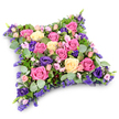 A serene and opulent floral pillow tribute is displayed, its cushion shape beautifully suggested by a dense covering of blossoms in pink, cream, and purple, all supported by fresh greenery. The dominant flowers are roses in varying moods of colour: some a striking fuchsia that adds vibrancy, others a soft and romantic blush pink, and several a creamy pale yellow, bringing warmth and light to the arrangement. Many are fully opened, allowing their layered, velvety petals to unfurl gracefully across the cushion's surface, while a few tighter buds hint at memories and stories still cherished. Among them, royal-purple lisianthus blooms add depth and a touch of solemn richness, their ruffled petals creating shadows and subtle movement. Scattered throughout, tiny clusters of lavender and lilac filler flowers, likely statice or limonium, fill every space, so the tribute looks luxuriously full and thoughtfully completed. A collar of foliage surrounds and threads through the flowers: rounded, silvery-green eucalyptus leaves offer a cool, calming note, and finer, darker fern-like greens soften the edges with feathery texture. The pillow appears as a neatly formed rectangle with rounded corners and a gentle dome, evoking the comfort of a final resting place and symbolizing eternal rest. Presented on a crisp white background, every colour and shape is clearly defined, allowing the eye to appreciate the care in each placement. This floral cushion feels perfectly suited to a memorial gathering in Stanmore, perhaps accompanied by family along Stanmore Hill or near local places of worship, conveying sympathy, remembrance, and a quiet wish for peace through the language of flowers.