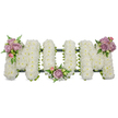 A tender, three-dimensional funeral tribute spells the word MUM in precise capital letters, each letter densely covered with hundreds of small, snowy-white spray chrysanthemums that form a cloud-like, velvety texture against a pure white background. The soft white petals give an impression of quiet, solemn light; their scent is faintly green and powdery, lending a gentle calm to the composition. Three small clusters of pastel blooms punctuate the design: a cluster of soft lavender roses with a single pale pink rosebud graces the upper left arm of the first M, another similar grouping nestles in the gentle curve of the central U, and a matching spray sits on the upper right arm of the final M. Fresh green foliage - slender fern fronds and brighter, glossy leaves - threads through and around those clusters, providing cool contrast and delicate movement. A dark green structural base, possibly wrapped in ribbon or moss, is visible beneath the flowers as a subtle outline that holds each letter upright and gives the tribute a dignified, anchoring depth. Bathed in even, soft light, the arrangement reads as an intimate, handcrafted memorial: the pristine white chrysanthemums symbolize peace and remembrance, while the lavender and blush roses add warmth and affection. This piece is conceived for a mother's funeral service, wake, or graveside dedication, created with the exacting care of a local florist who knows how to balance reverence and beauty. The overall mood is one of serene respect, a comforting visual embrace for those gathering to remember and to honour a beloved mum.