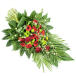 A thoughtfully crafted sympathy spray is shown laid out on a bright white background, highlighting every nuance of its red and green palette. The composition follows a smooth, elongated teardrop line, wide and full through the centre and gracefully narrowing at both ends - a classic shape for a casket spray or front-facing funeral tribute often requested by families in the Stanmore area. At its heart, a dense cluster of deep red roses forms the main focal point, their velvety petals appearing almost plush to the touch. These roses are joined by matching red gerbera daisies with dark eyes and ruffled carnations, all harmonising in a rich, solemn crimson that conveys love, honour, and remembrance. Threaded among the red flowers are lime-green button chrysanthemums, their small, rounded pompon heads adding both visual texture and a refreshing contrast, like bright notes of new growth against the more sombre tones. Throughout the length of the arrangement, delicate white filler blooms - tiny, star-like flowers reminiscent of gypsophila or miniature daisies - bring lightness and a gentle, airy feel. A generous bed of foliage supports and frames the flowers, with broad, glossy dark leaves giving the piece structure and feathery ferns and other mixed greens creating soft, layered depth. On the lower right side, several long, slender palm-like leaves fan outward in an elegant sweep, reinforcing the elongated shape and adding a sense of movement. At the upper left, a neat bundle of upright green stems, artfully wrapped at the base with a single broad leaf, provides height and a contemporary accent. The overall effect is of a balanced, dignified funeral spray, offering a quiet yet eloquent expression of condolence.
