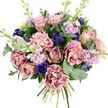 A lush, hand-tied bouquet is shown against a plain white background, the neutral setting allowing each flower and texture to stand out with clarity. At the centre, full-blown garden roses in blush pink, dusty rose, and soft mauve unfurl their layered petals, creating a sense of gentle romance that would feel perfectly at home in a Stanmore bay window. Around them, ruffled carnations add pleasing fullness and movement; their petals blend from creamy, pale interiors to deeper pink, fuchsia, and plum-toned tips, giving each bloom a slightly different character and a soft, fabric-like appearance. Threaded between the pinks are rich indigo blossoms, neat and bud-like, reminiscent of small tulips or tightly closed anemones, adding pockets of dramatic, cool-toned colour. Near the bottom-front of the bouquet, one open royal blue anemone steals attention, its velvety petals circling a dark, almost black centre that acts as a natural focal point. Long, slender stems of lilac and pale lavender stock rise gently through the design, their clusters of tiny flowers introducing height, a light, airy texture, and an imagined scent: softly floral with a hint of spice, like the fragrance that drifts from gardens around The Common in Stanmore on a mild evening. Embracing the blooms is a mix of rounded silvery eucalyptus and rich green foliage, which frame the colours and suggest a cool, clean freshness. The visible, neatly bound stems at the base show that this is a freshly made hand-tied arrangement from a local Stanmore florist, ready for delivery to homes near Stanmore station or the quiet roads off Marsh Lane. The bouquet's overall mood is soothing, elegant, and deeply thoughtful, ideal for anniversaries, comforting gestures, birthdays, or simply to add a note of refined beauty to everyday life.